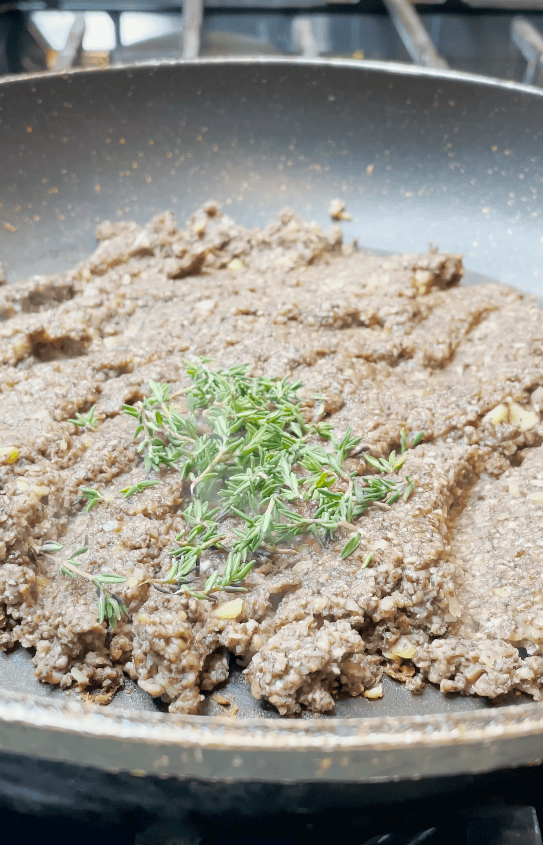 Rosemary on cooking mushrooms in a skillet.