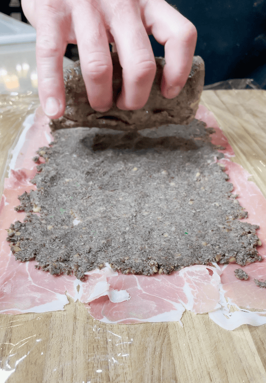 Placing meat onto mushroom and prosciutto.
