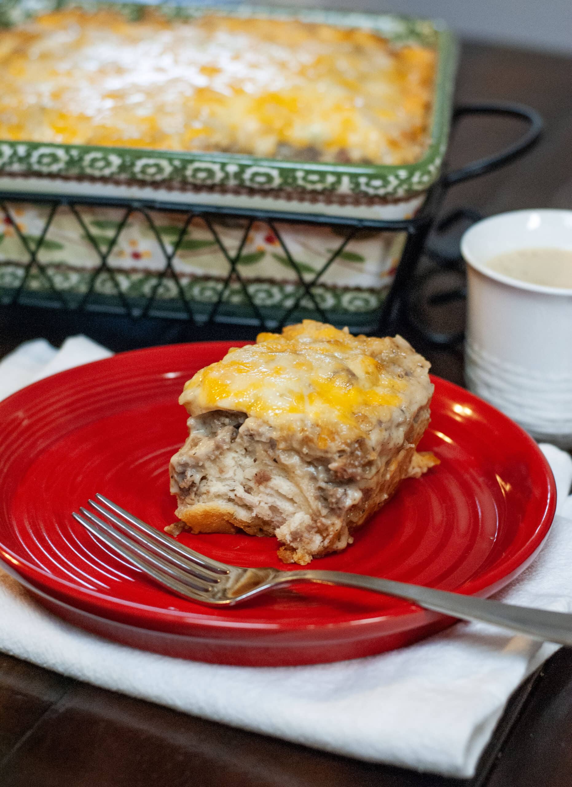 A slice of breakfast casserole on a red dish next to a cup of coffee.
