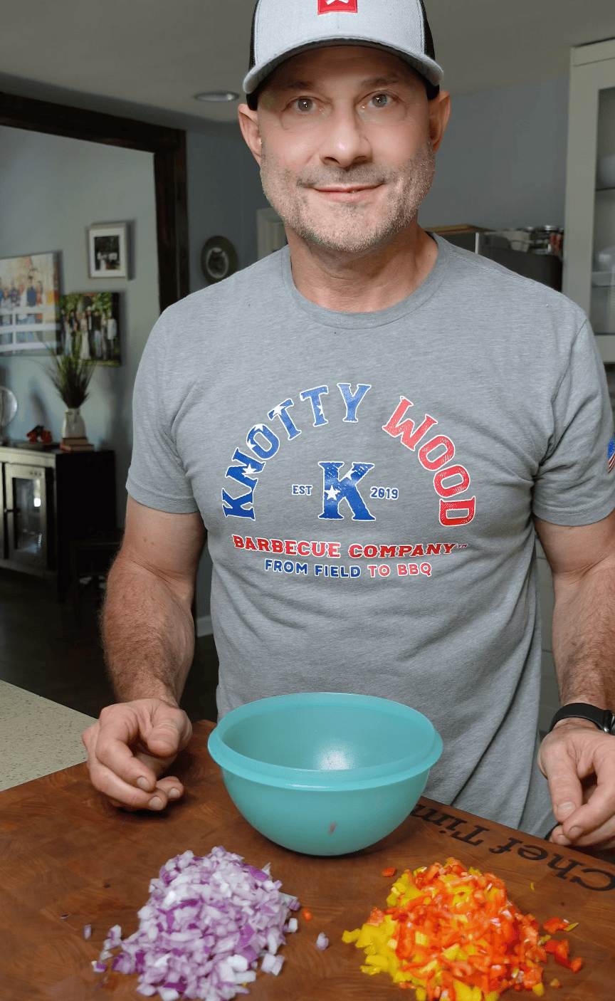 Tim adding peppers and onions into a blue bowl with a wooden cutting board underneath. 