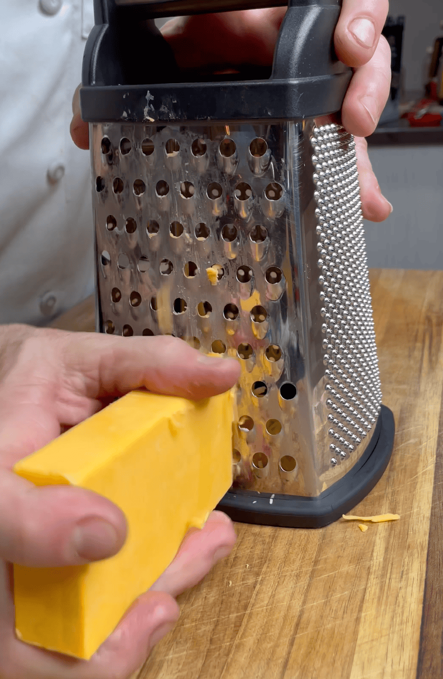 A cheese grater with a hand grating cheddar cheese. 