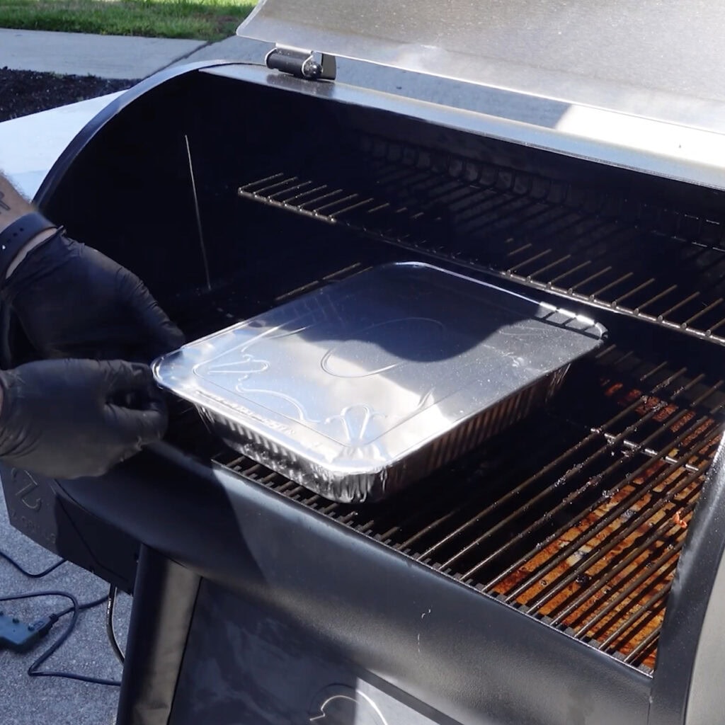 Pork burnt ends being placed on the smoker with a cover on them.