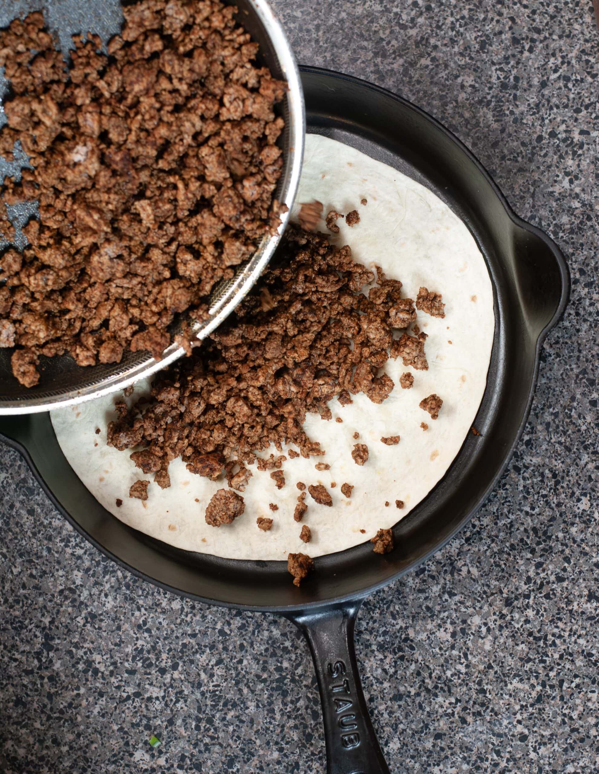 Meat on a tortilla in a cast iron skillet.