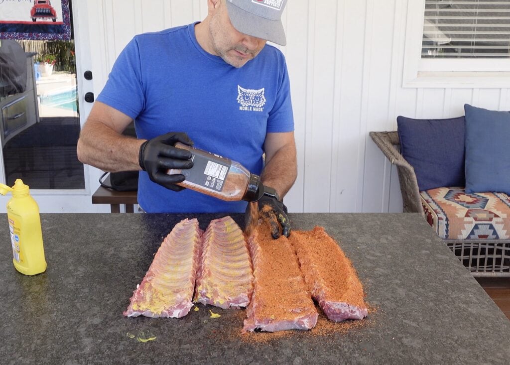 Ribs being seasoned with pig rub.