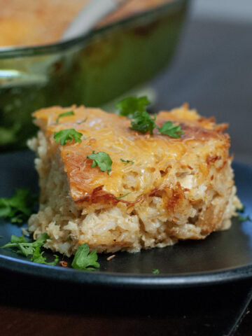 A slice of casserole with rice on a black plate.
