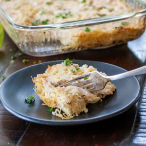 Chicken tetrazzini on a blue plate next to a casserole dish.