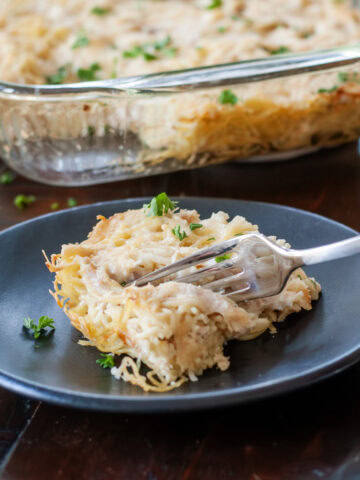 Chicken tetrazzini on a blue plate next to a casserole dish.