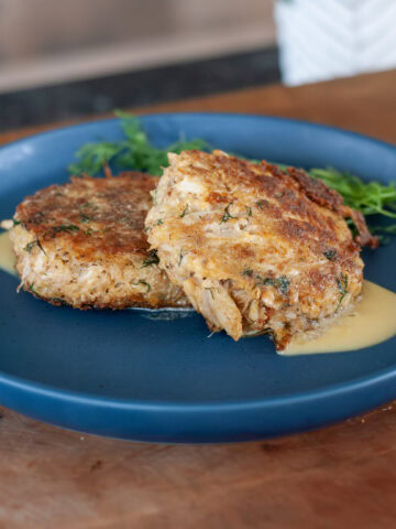 Two crab cakes on a blue plate with a butter sauce.