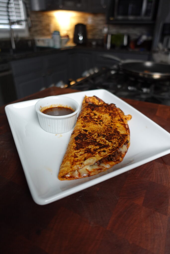 A birria taco plated with a dipping sauce.