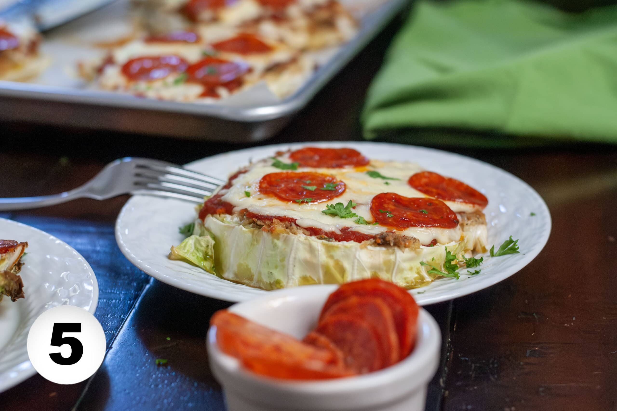 Cabbage pizza on a plate with pepperoni's and a fork.