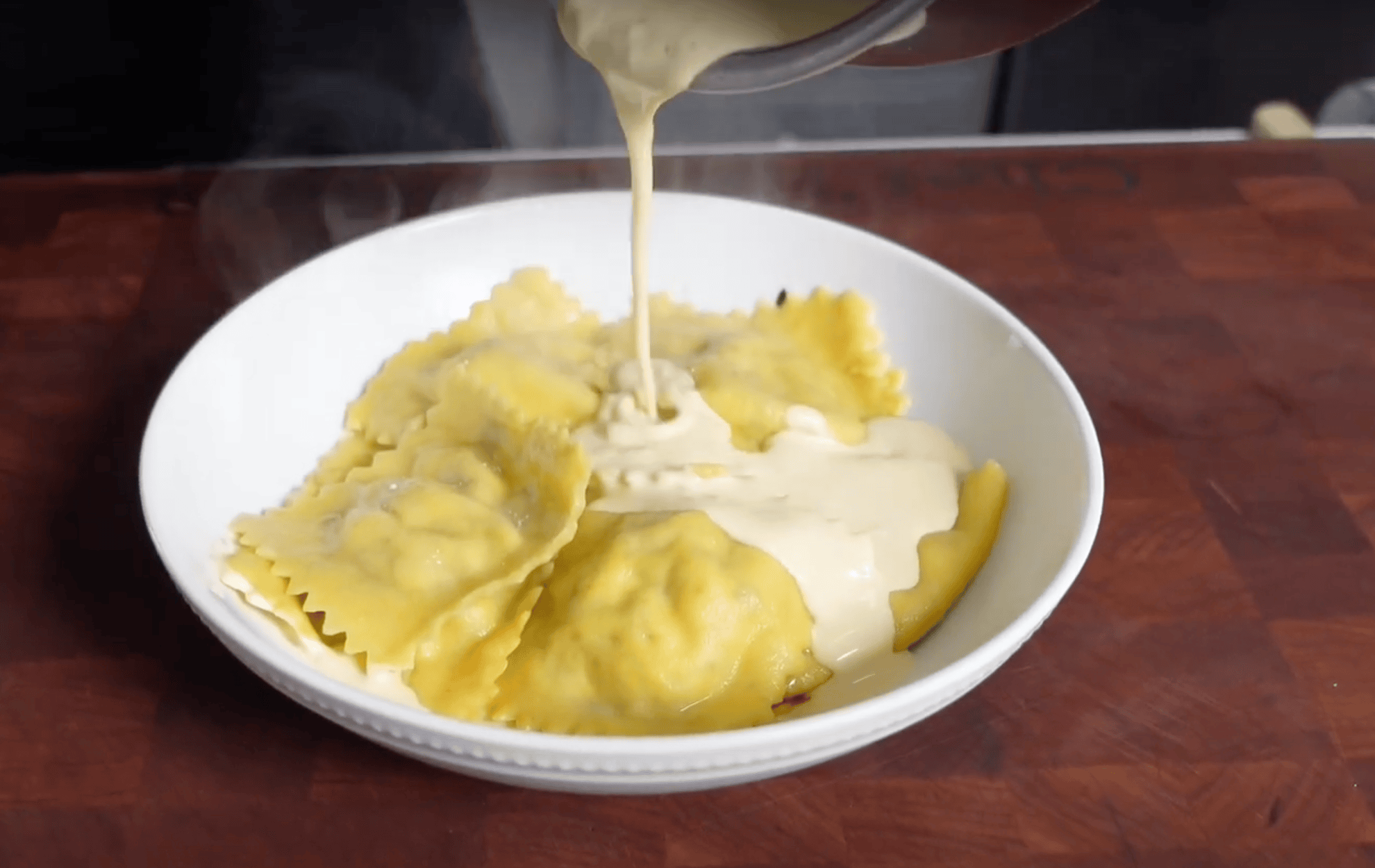 Cream sauce pouring over ravioli.