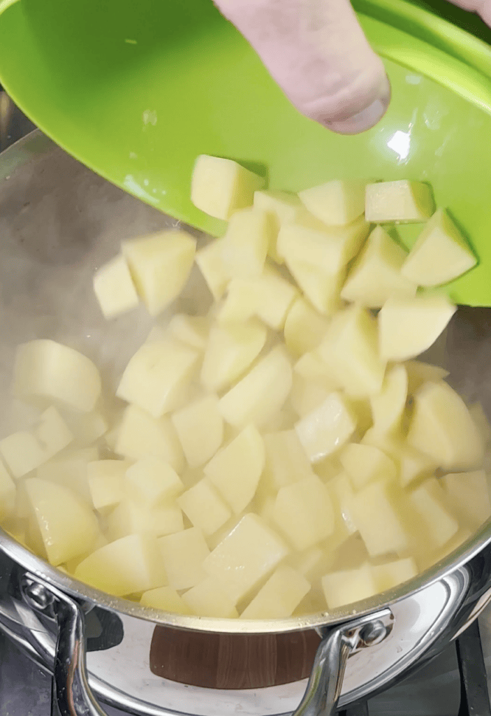Potatoes going into a pot of water.