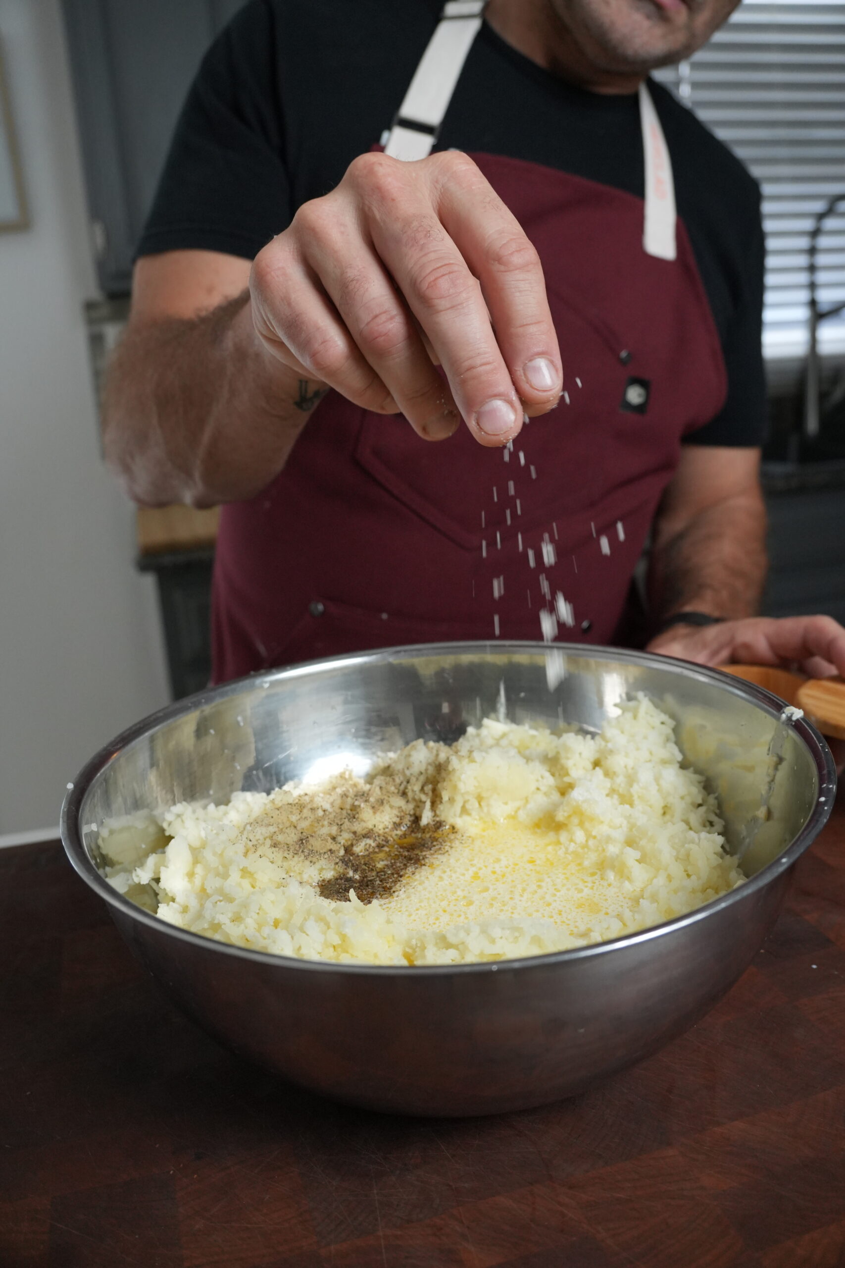 Salt going into a bowl with potatoes and butter cream.