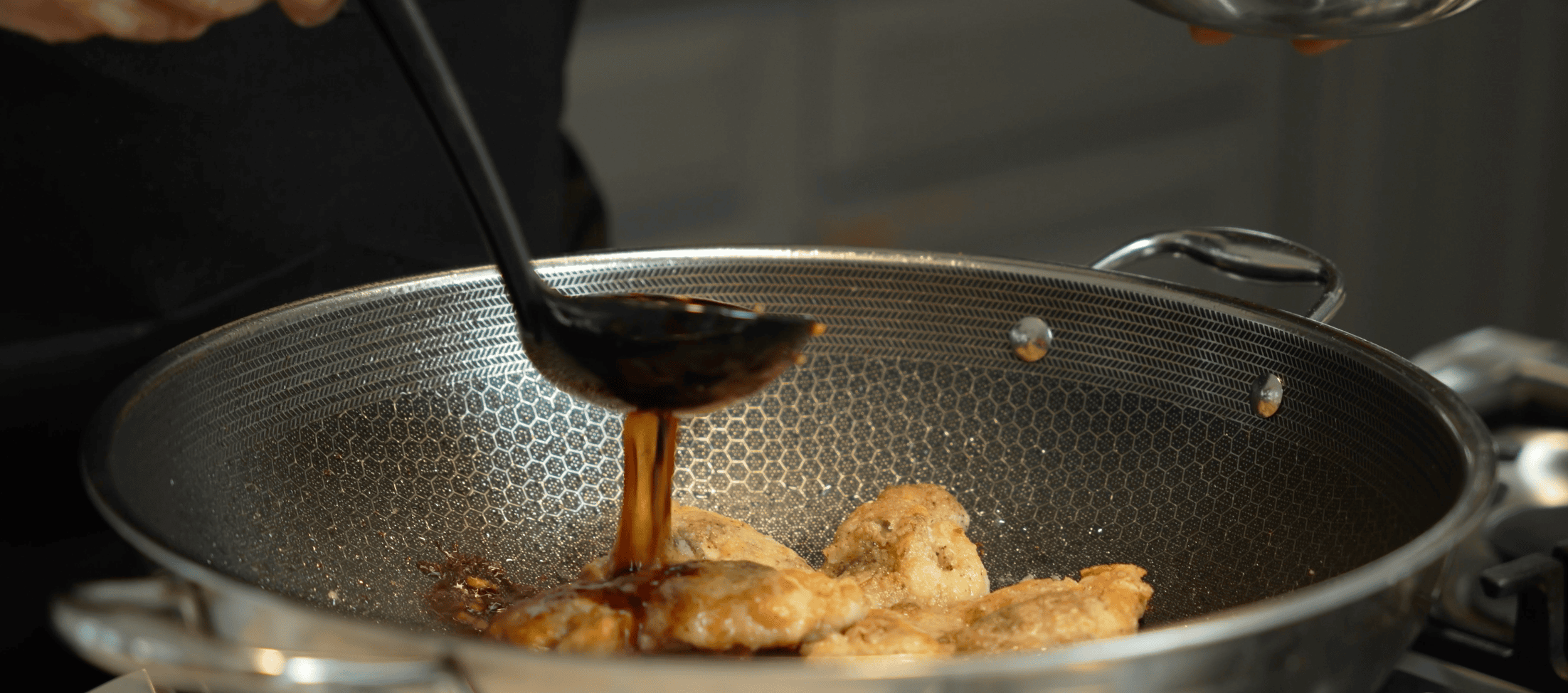 Teriyaki sauce pouring over chicken in a wok.