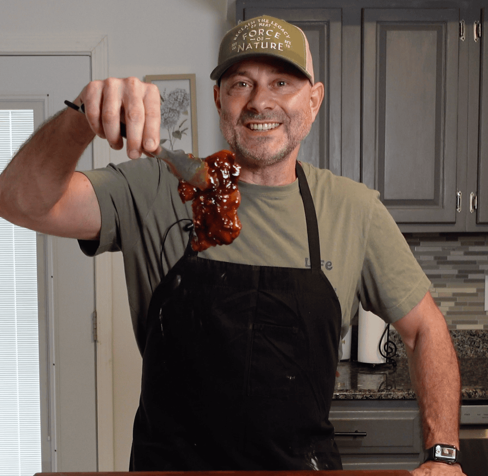 Tim holding up a piece of teriyaki chicken with tongs.