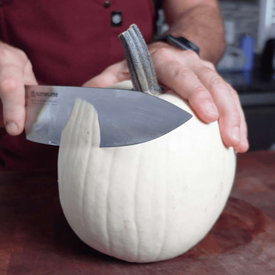 A man is cutting a white pumpkin with a knife.