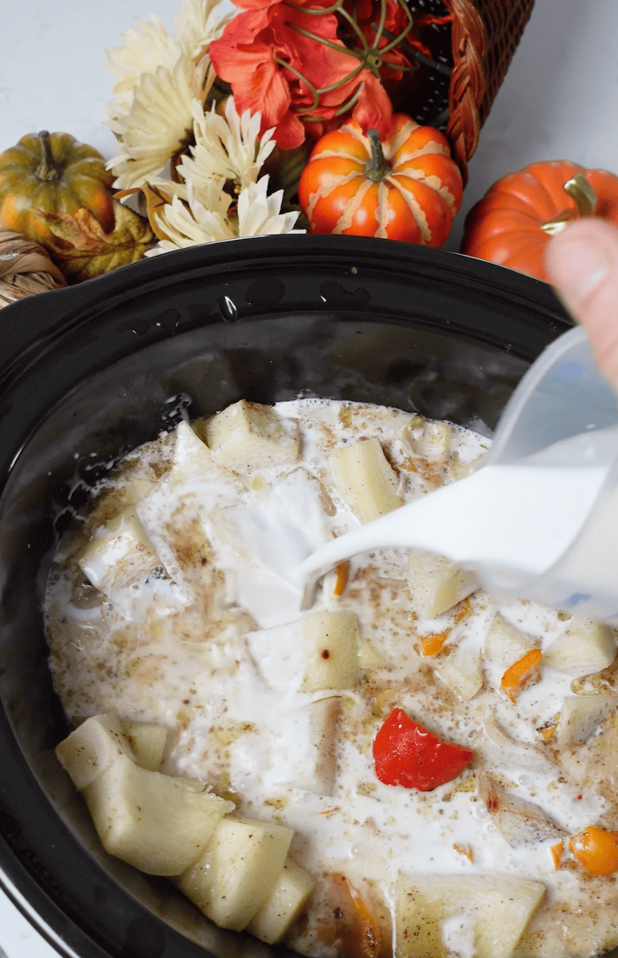 Heavy cream pouring into crockpot with soup.