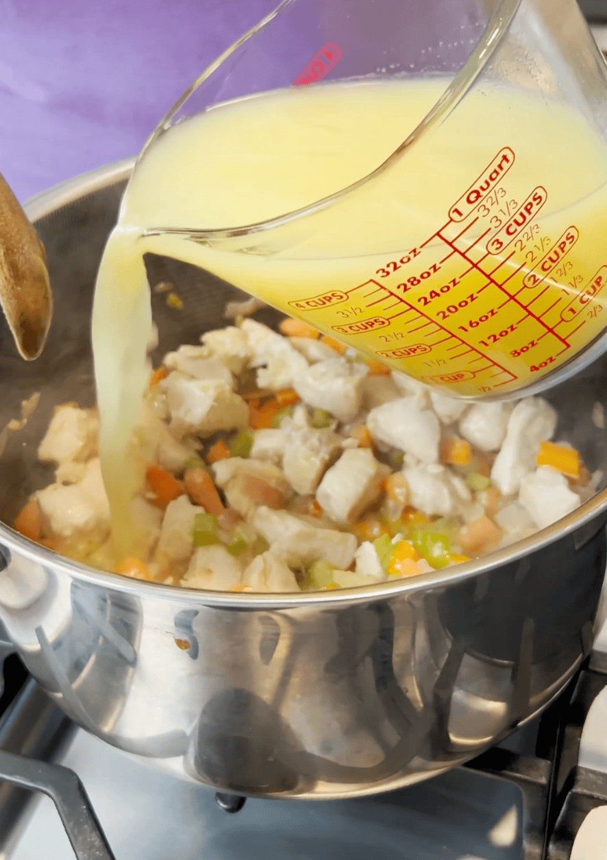 Chicken broth pouring into a pot on the stove.