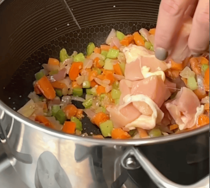 Chicken going into a pot with chopped vegetables.