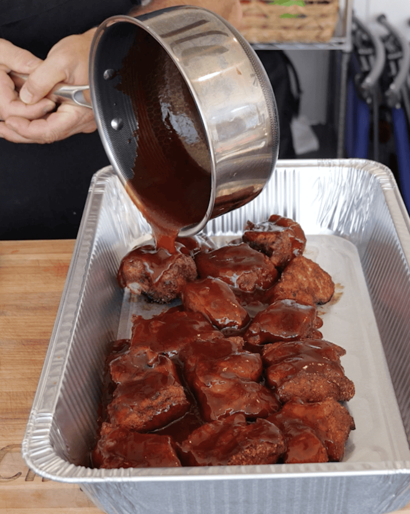 BBQ Sauce pouring over meat in a pan.