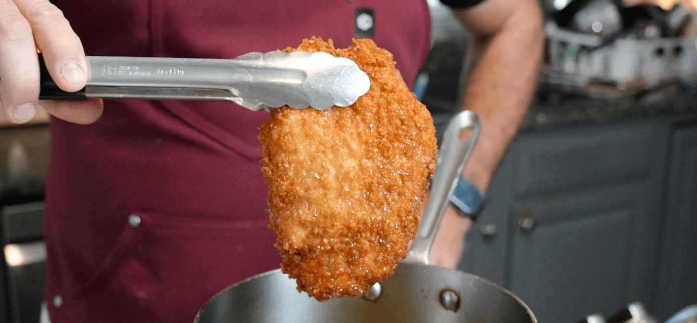 Tongs holding up a piece of crispy chicken tenders. 