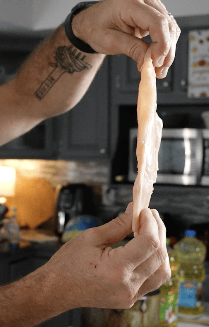 Two hands holding up a piece of chicken breast. 