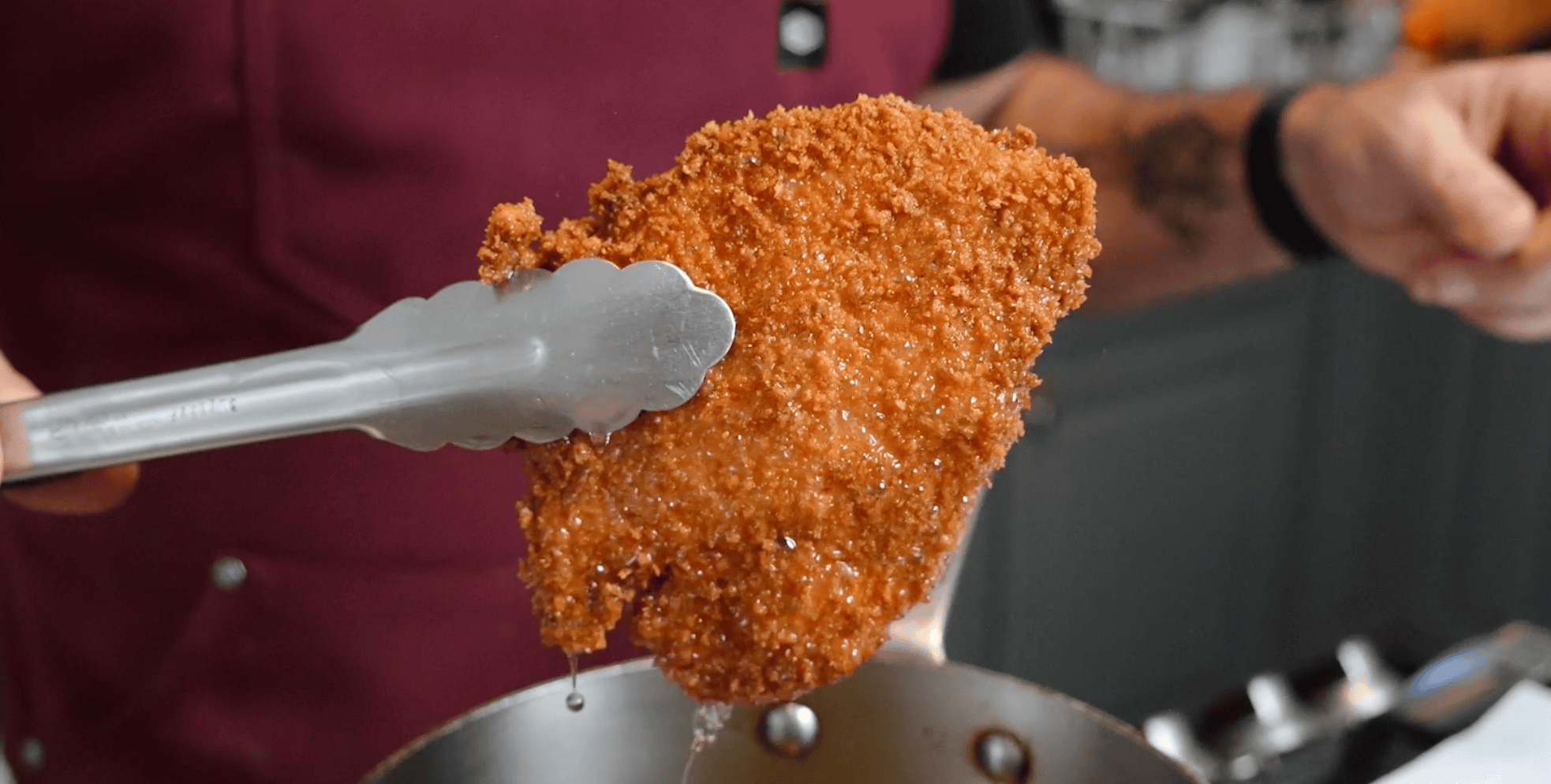 Tongs holding up a fried chicken tender. 