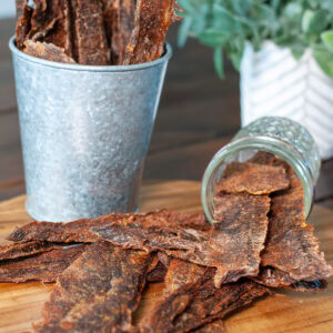 Beef jerky on a platter with small metal tongs.