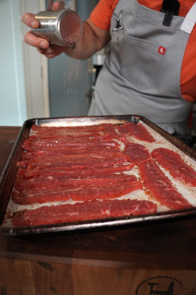 Beef jerky being seasoned with salt, pepper, paprika, onion and garlic powder.