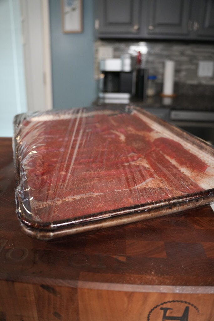Beef jerky on a cooking sheet with plastic wrap.