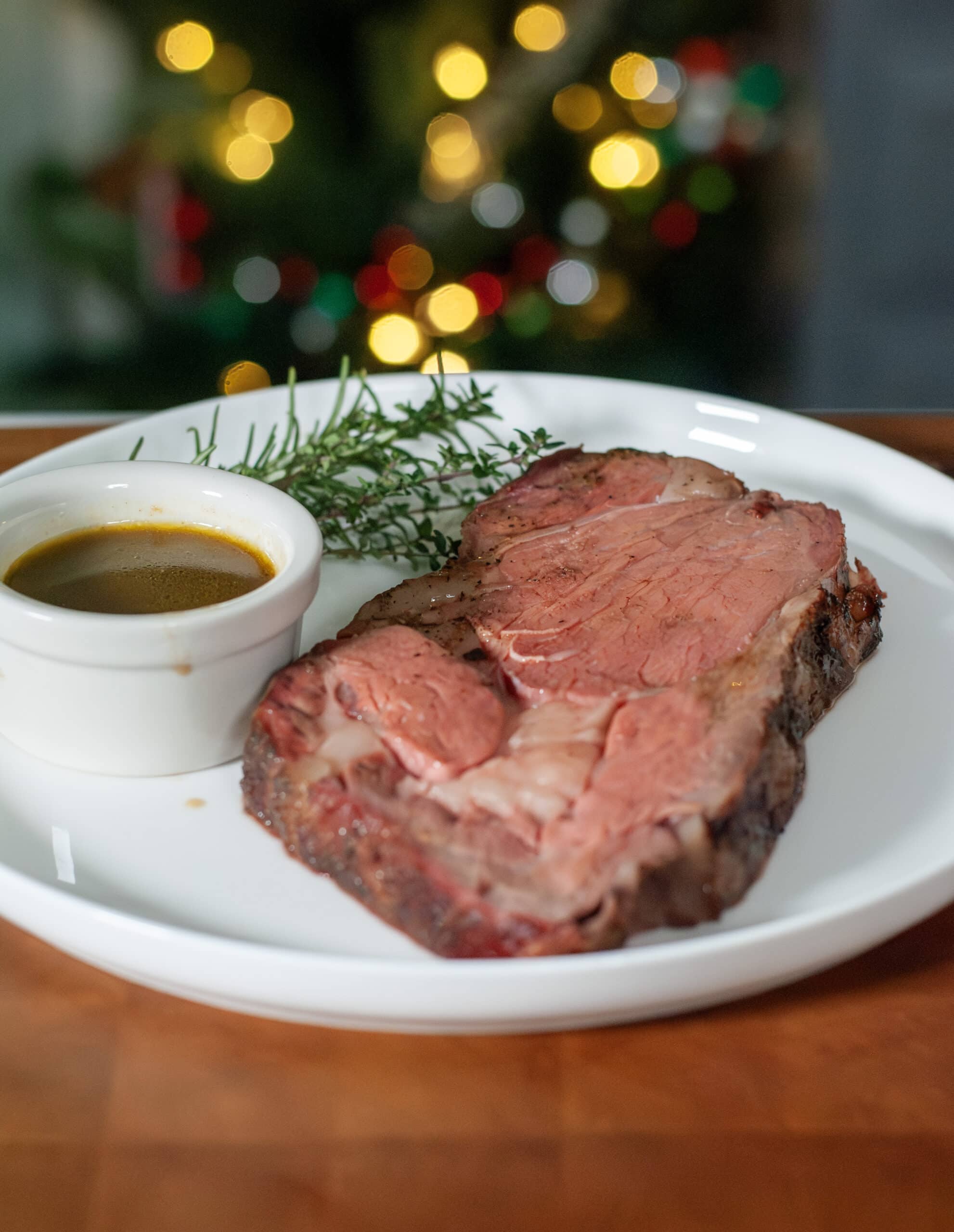 A slice of prime rib on a plate by a lit up tree.