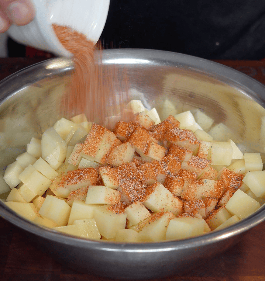Seasoning going onto chopped potatoes.
