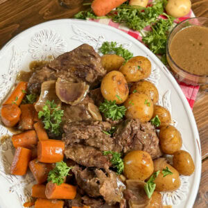 Baby potatoes, chopped carrots, parsley and cooked roast on a white plate.