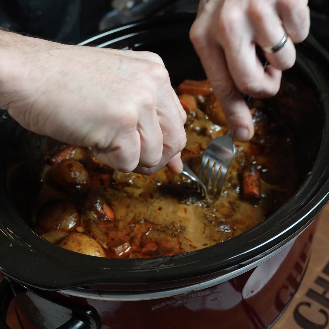 A fork pulling apart meat in a crock pot.