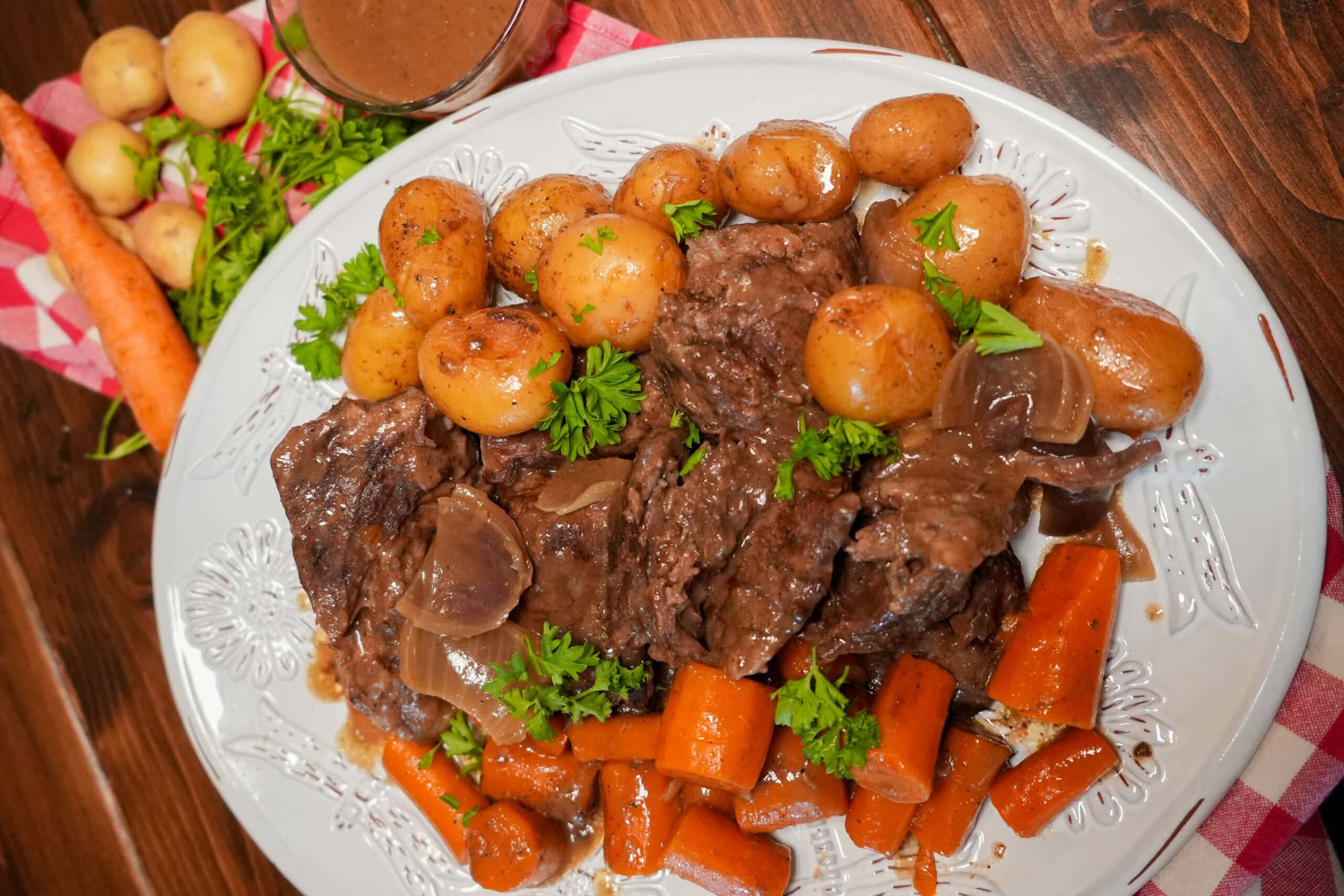 A cooked roast on a plate with chopped carrots and potatoes and parsley.