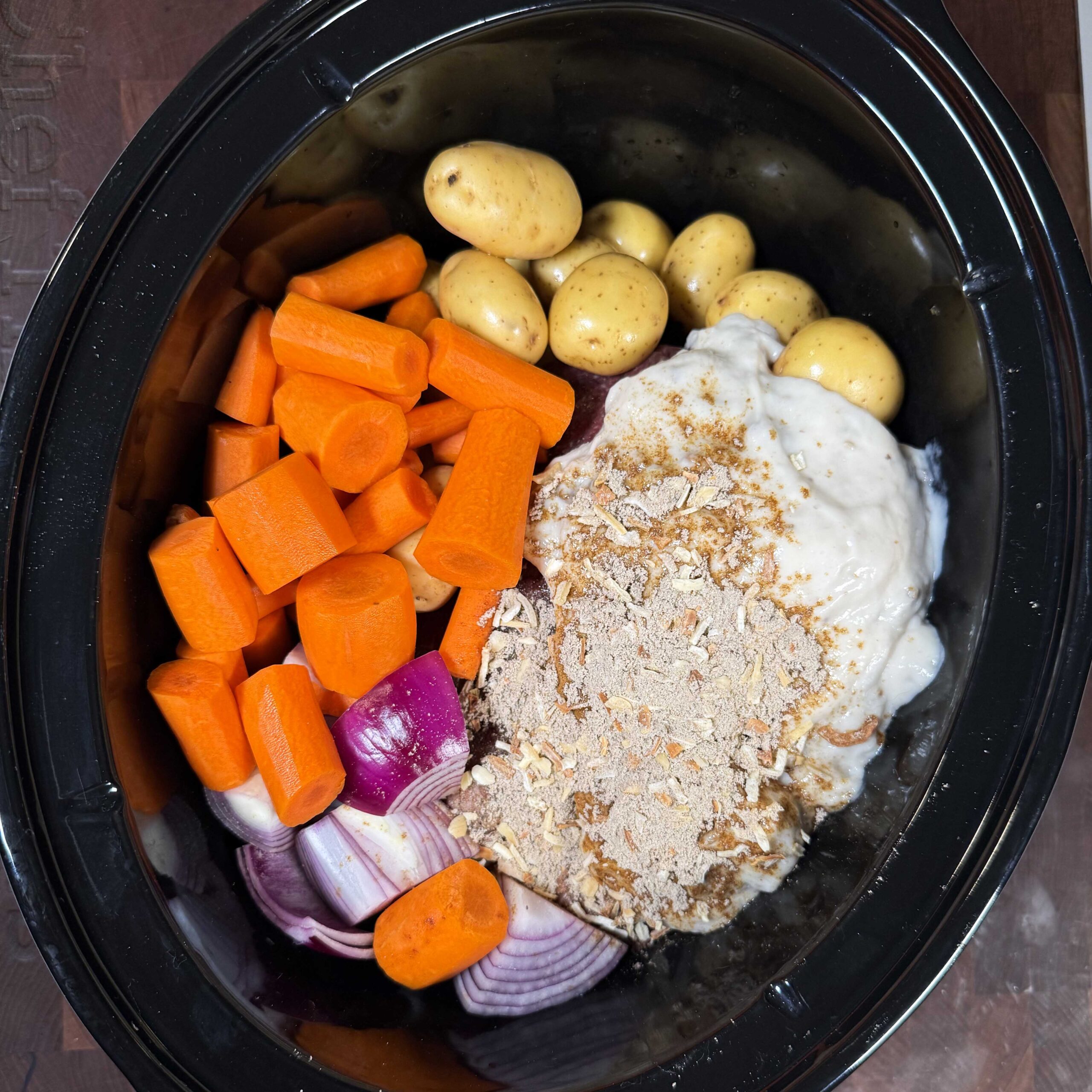 Ingredients for pot roast sectioned off in a black crock pot.