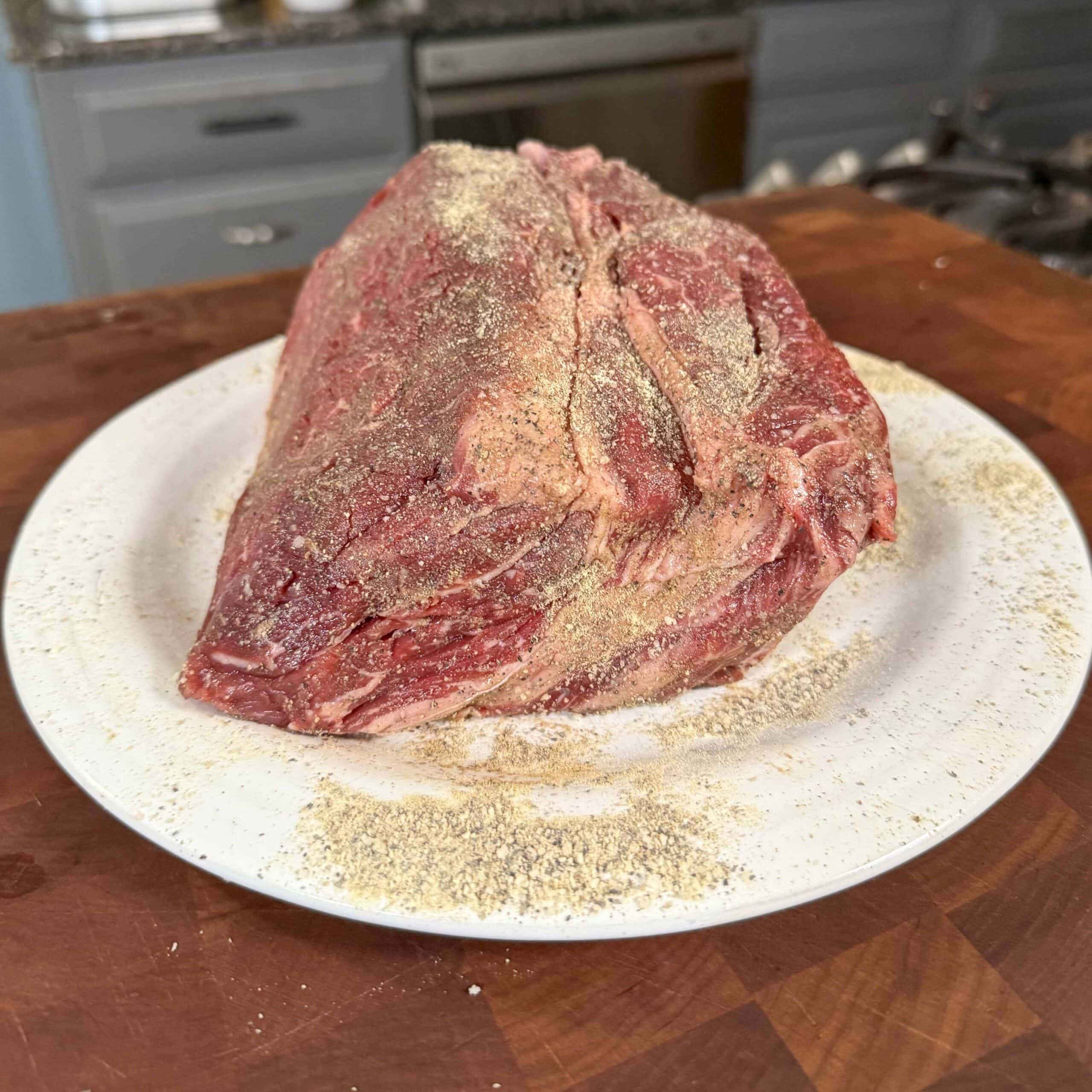 Seasoned pot roast on a white plate ready for the crockpot.