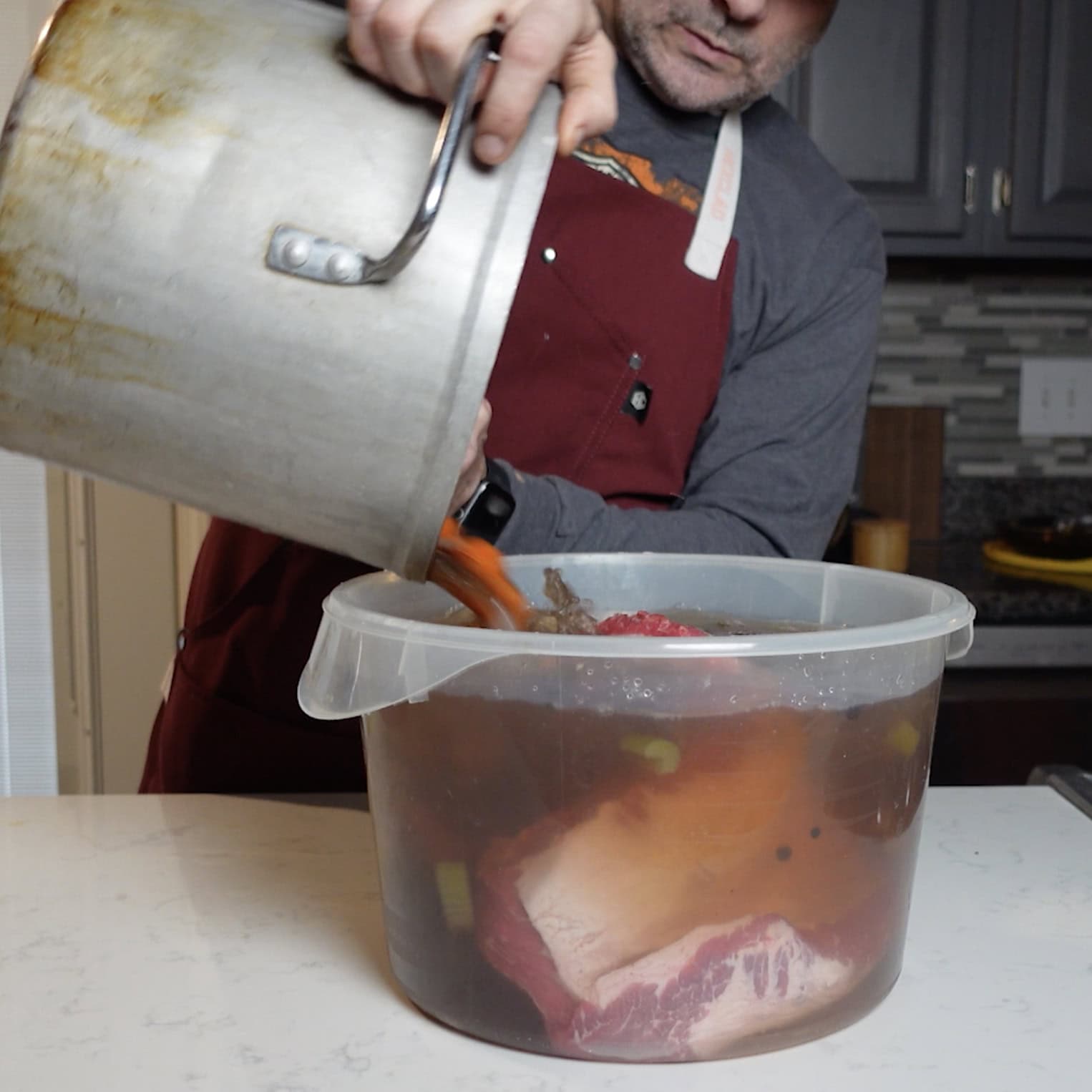 Brine is being poured over the brisket in a large container.