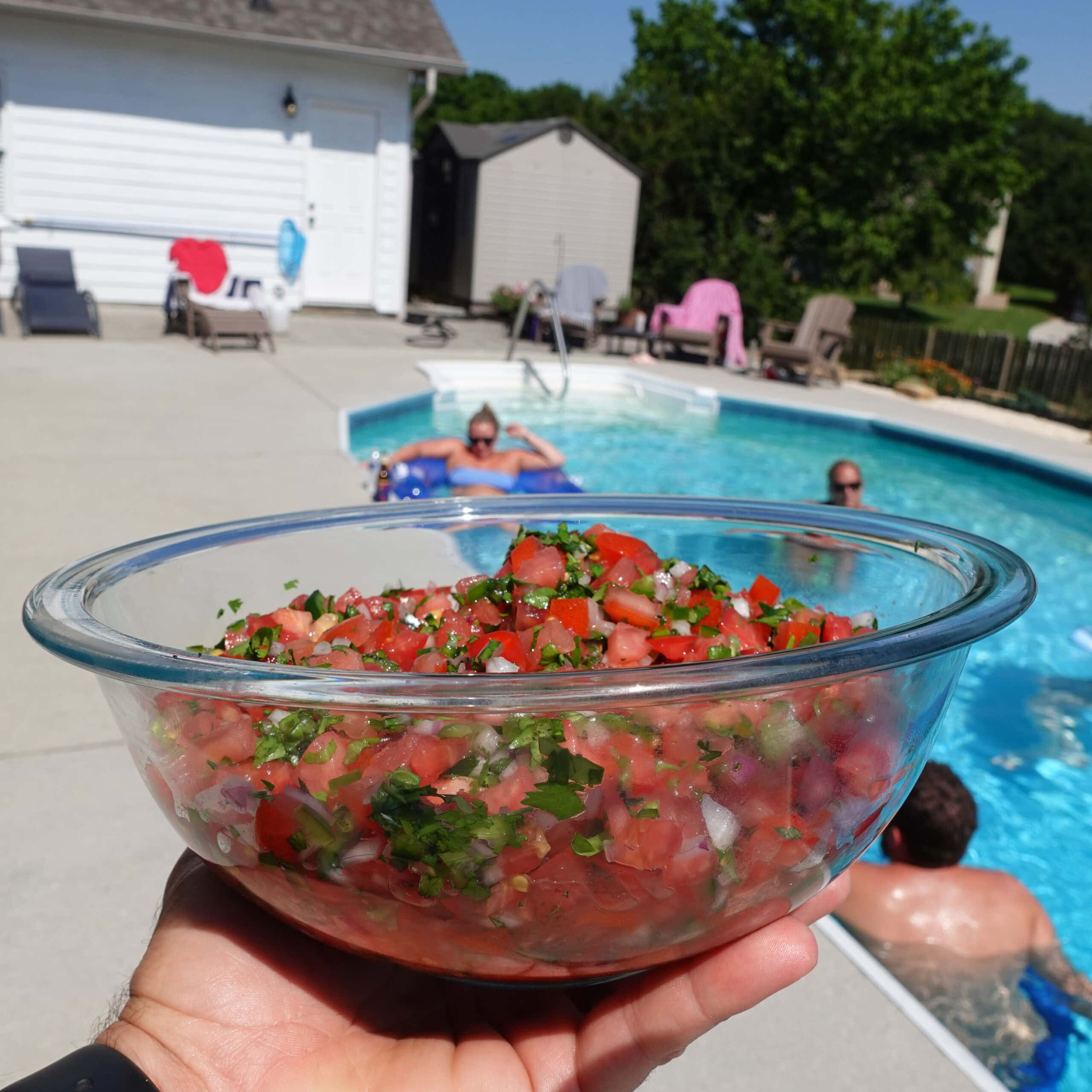 A fresh bowl of salsa next to a pool area.