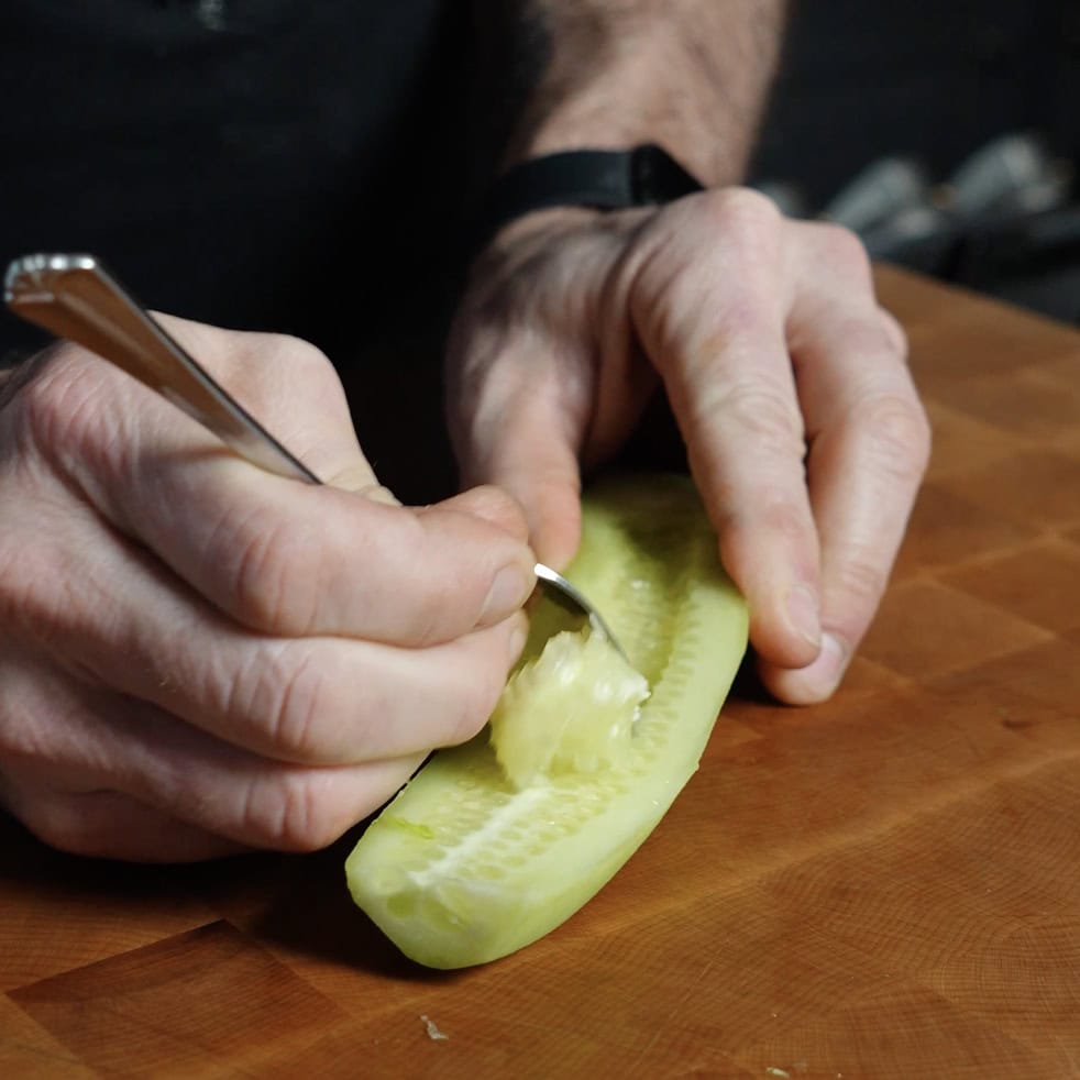 Removing the seeds from a cucumber with a spoon.