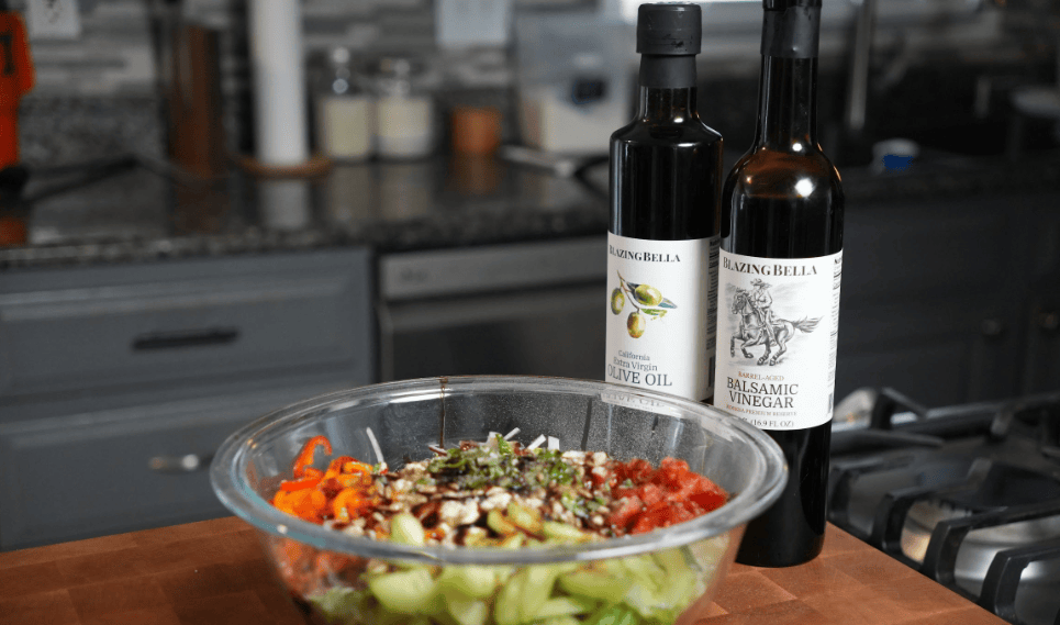 A bowl of salad next to Blazing Bella olive oil and vinegar.
