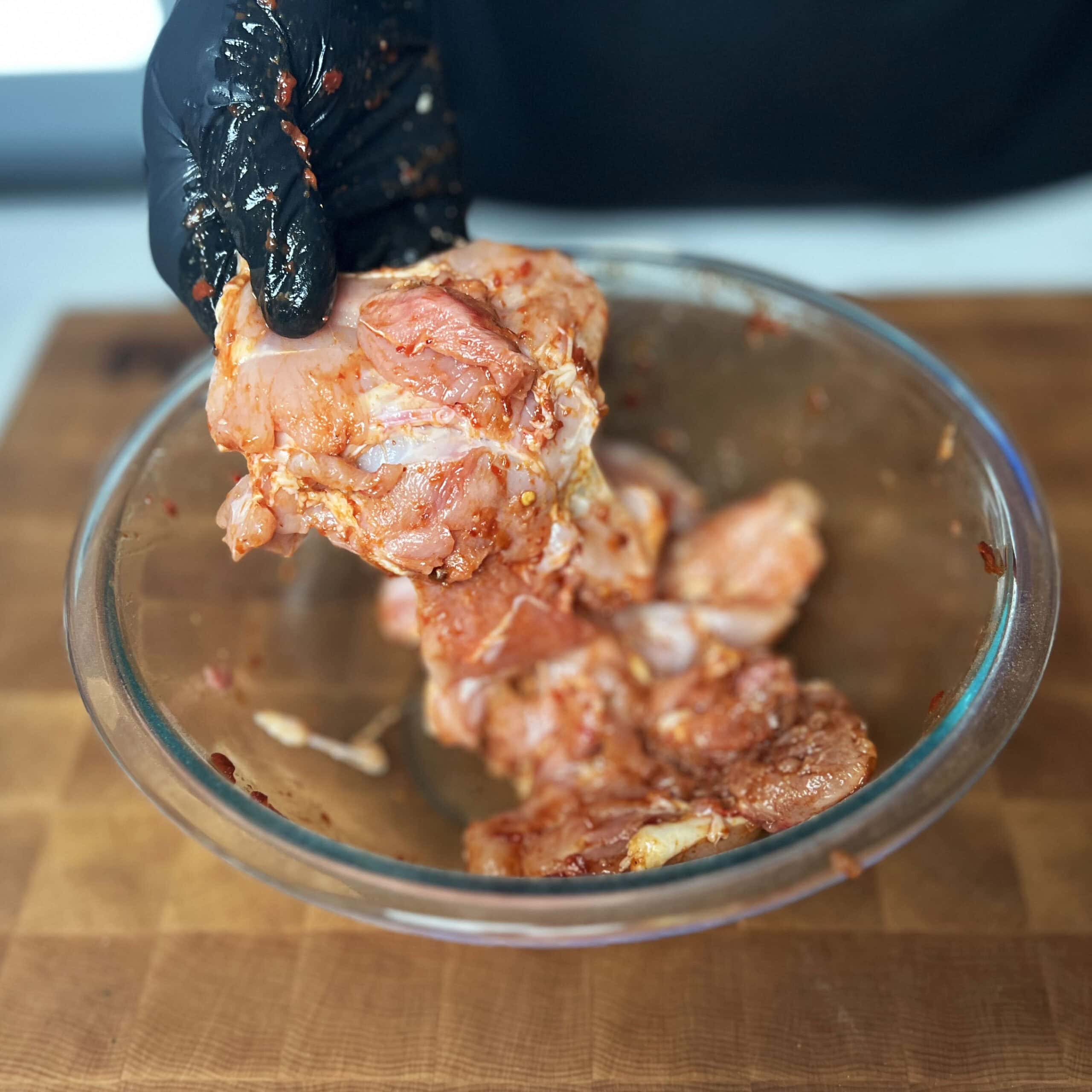 Chicken being seasoned shown in a glass bowl. 