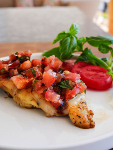 Bruschetta chicken on a white plate with drizzled balsamic vinegar.