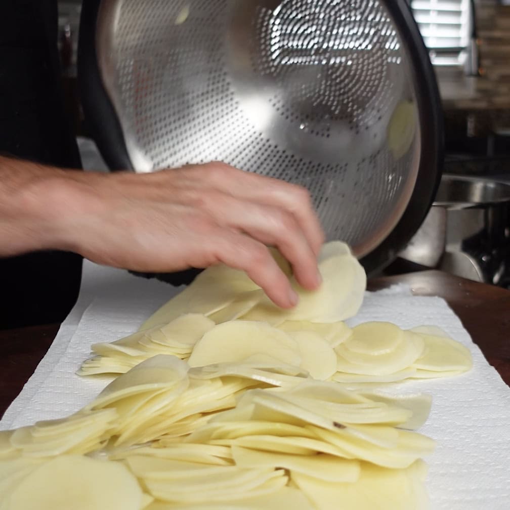 Sliced potatoes coming out the strainer onto a paper towel.