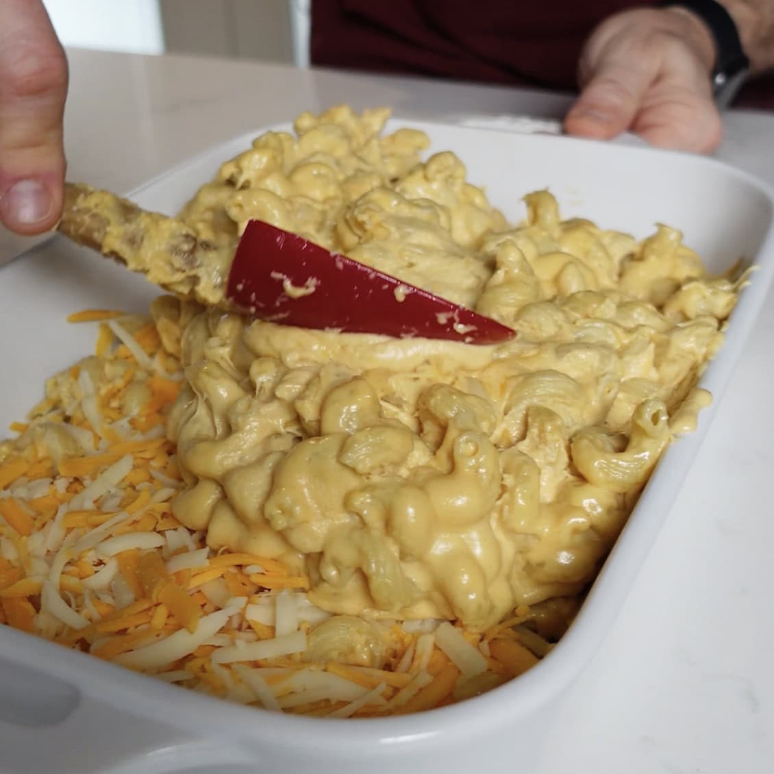 Spreading Mac and cheese over a Layer of cheese in a baking dish.
