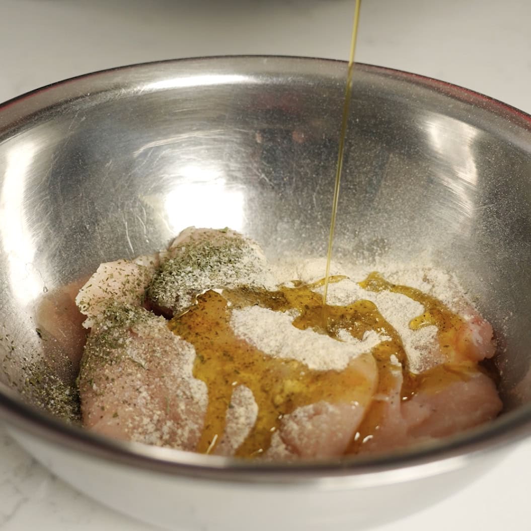 Seasoning chicken in a silver bowl.