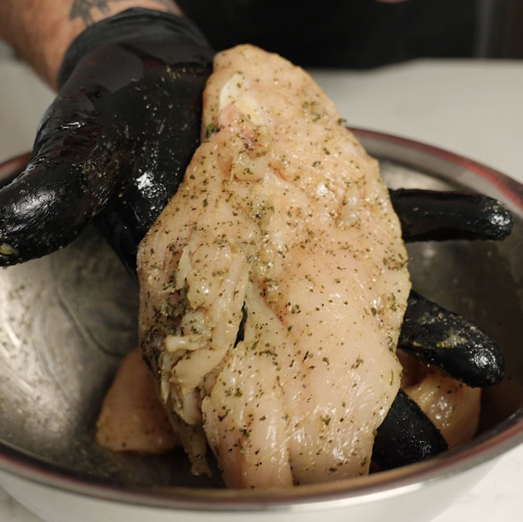 Seasoned chicken in a silver mixing bowl.