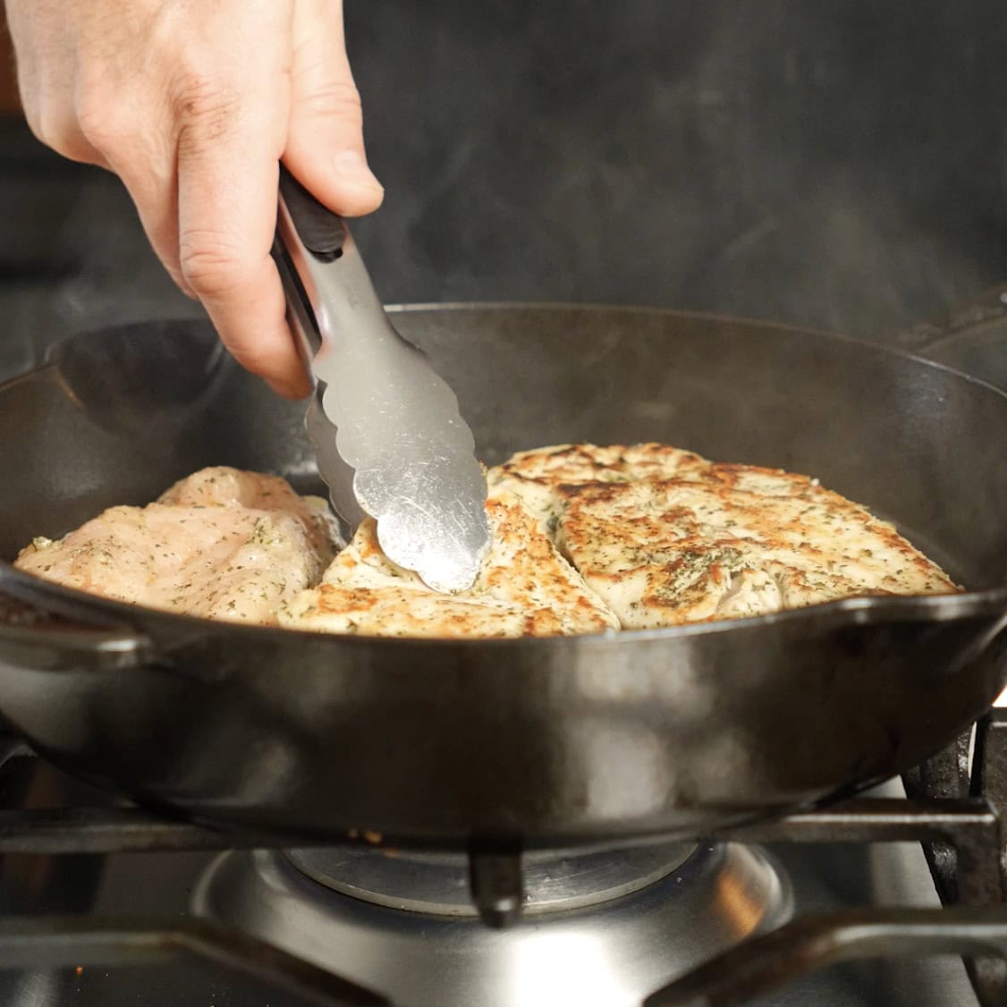 Flipping chicken on a skillet with tongs.