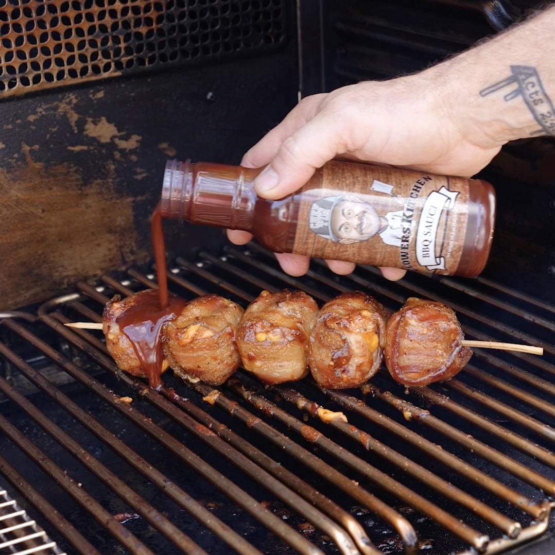 Pouring chef tims bbq sauce onto the smoked thighs on the smoker.