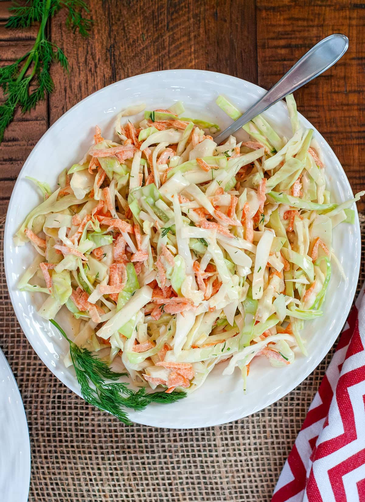 A bowl of fresh slaw showing shredded cabbage, carrots, fresh dill with a creamy dressing.  Some fresh dill on the side of the bowl. 